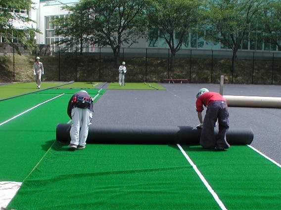 砂入り人工芝を展開して設置する施工工程の様子