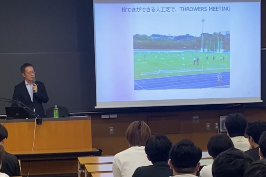 法政大学多摩キャンパスで投てき競技ができる人工芝グラウンドについて講義する越後幸太郎社長