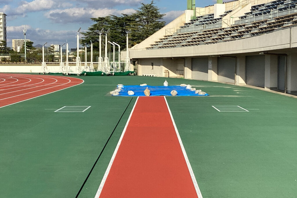 赤色の全天候１レーンの助走路とグリーンのアウトフィールドの写真