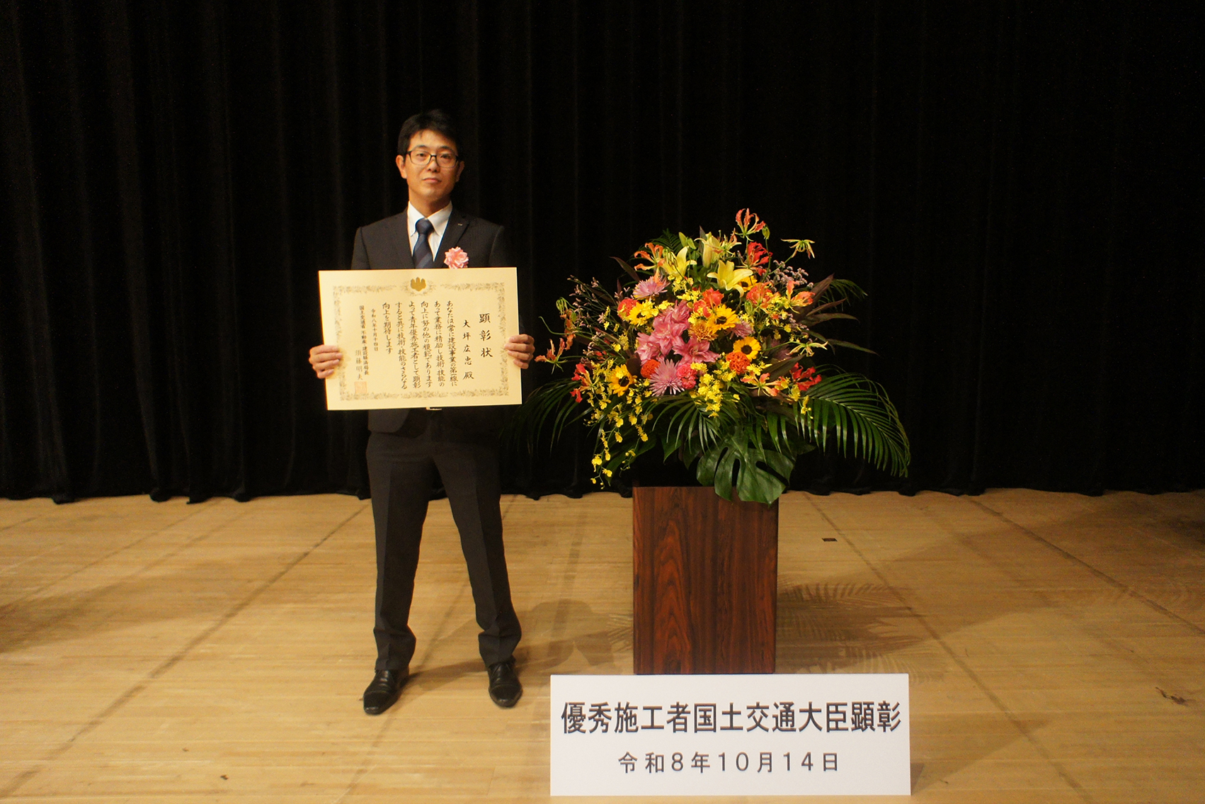 花束の前で賞状を持って記念撮影